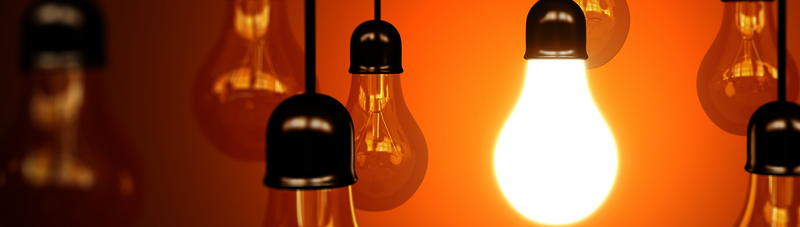 Glühbirnen hängen vor einem orangefarbenen Hintergrund, eine leuchtet