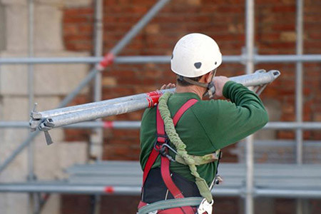 Bauarbeiter trägt Stahlrohre auf seiner Schulter