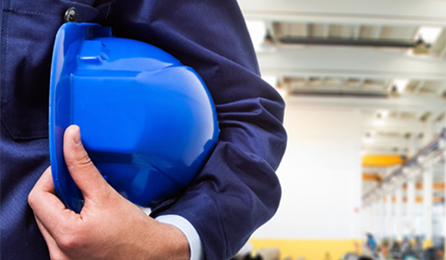 Mann im Blaumann mit blauem Schutzhelm unter dem Arm in einer Fabrikhalle; © Minerva Studio - Fotolia.com
